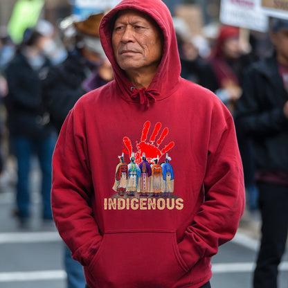 an old man wearing a red hoodie with the word indigenous on it